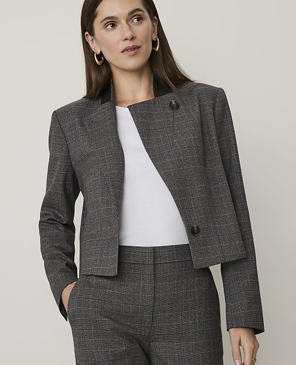 A woman in a plaid blazer and pants stands against a plain background.