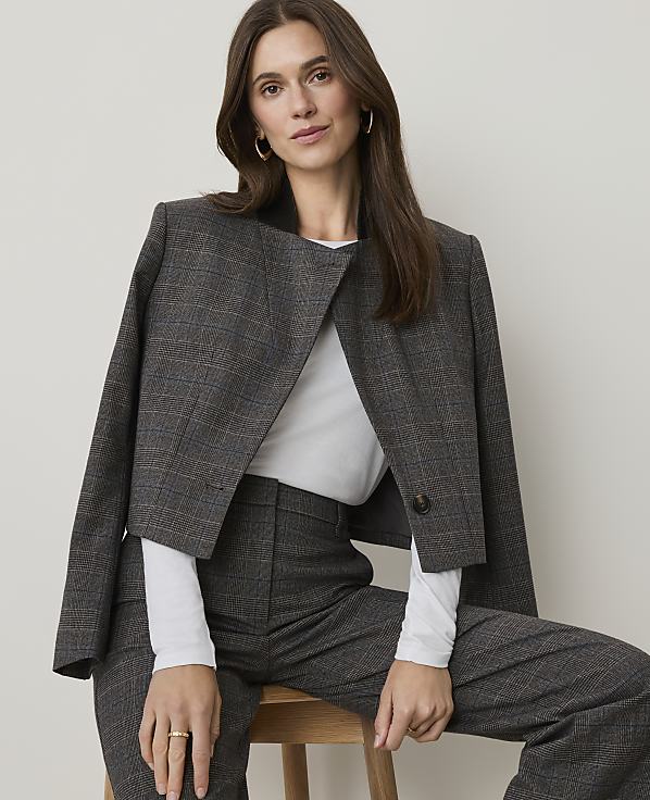 A woman in a plaid suit sits against a plain, light-colored background.