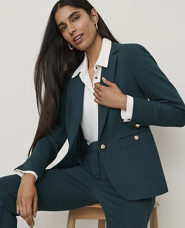 A woman in a teal blazer and pants poses against a plain, light background.