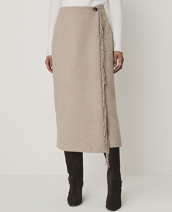 A beige wrap skirt with fringe detailing is worn over dark boots against a plain white background.