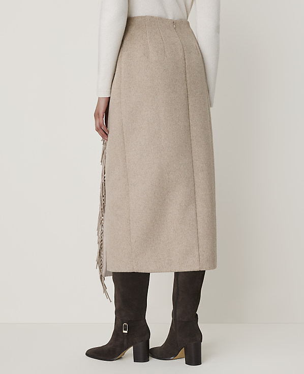 A beige midi skirt with fringe detailing is worn with dark brown boots against a plain white background.