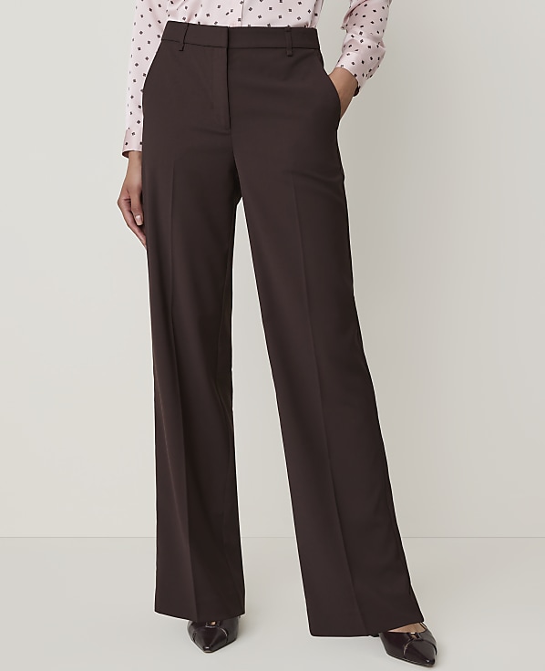 A person in a pink polka dot shirt and brown wide-leg trousers stands against a plain white background.
