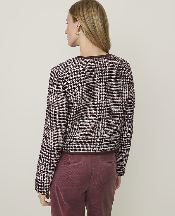 A woman in a plaid jacket and maroon corduroy pants stands against a plain, light-colored background.