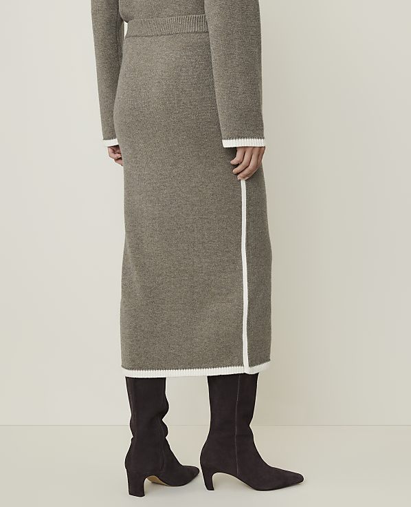 A person wearing a taupe knit midi skirt and dark brown boots stands against a plain, light background.
