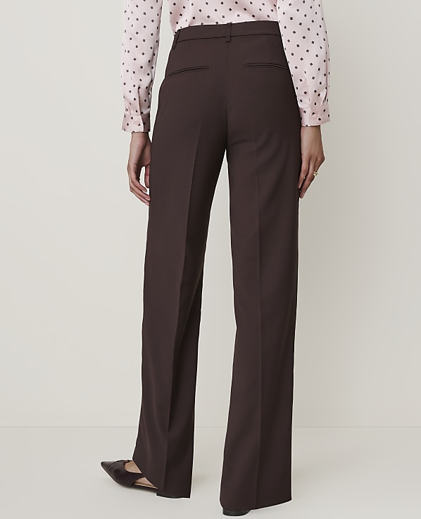 A person wearing brown wide-leg trousers and a pink polka-dot blouse stands against a plain, light-colored background.
