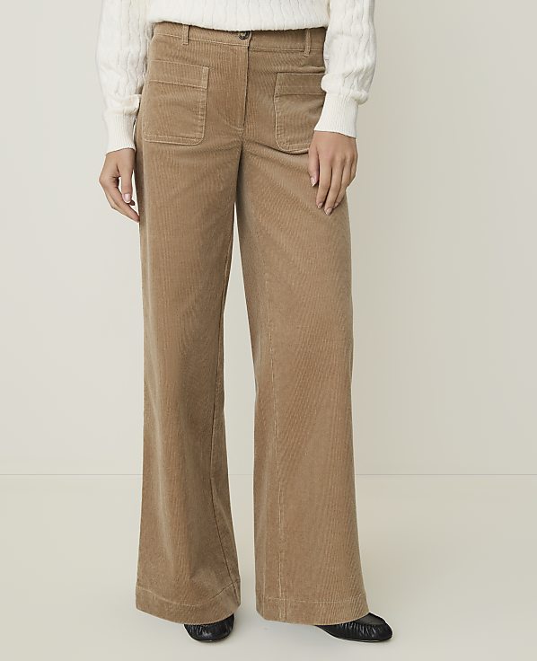 A person stands in wide-leg corduroy pants and a white sweater against a plain, light background.