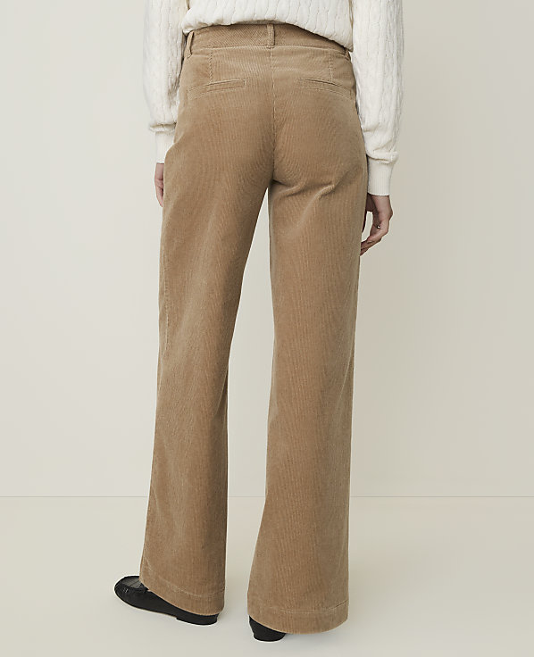 A person wearing tan corduroy pants and a white sweater stands against a plain, light-colored background.