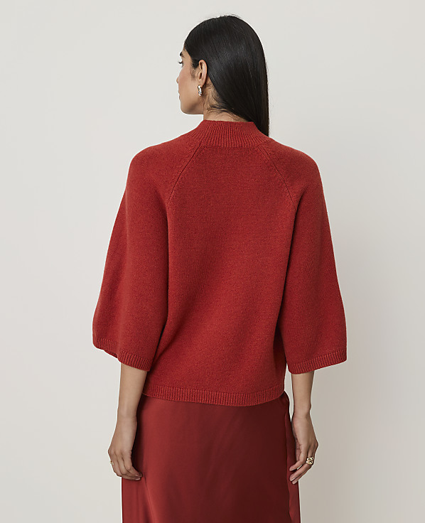 A woman in a rust-colored sweater and skirt stands against a plain white background.