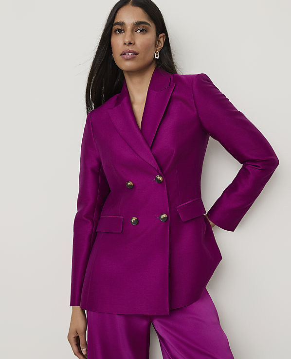 A woman in a vibrant magenta blazer and matching pants stands against a plain, light background.