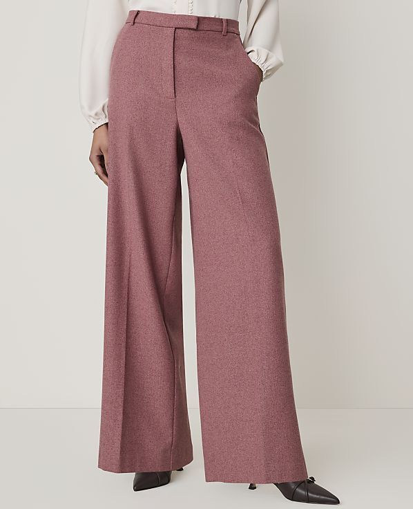 A person stands in wide-leg pink trousers and a white blouse, with a plain white background.