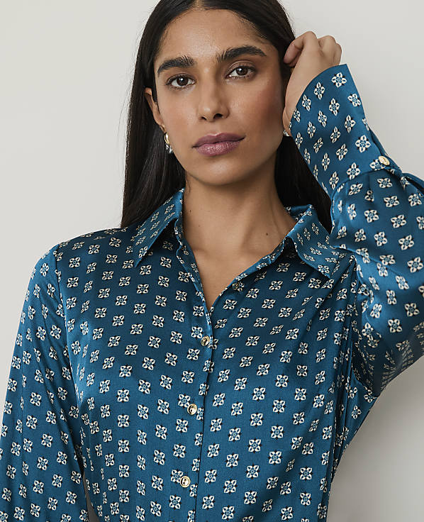 A woman with dark hair and a patterned teal shirt is shown against a plain white background.