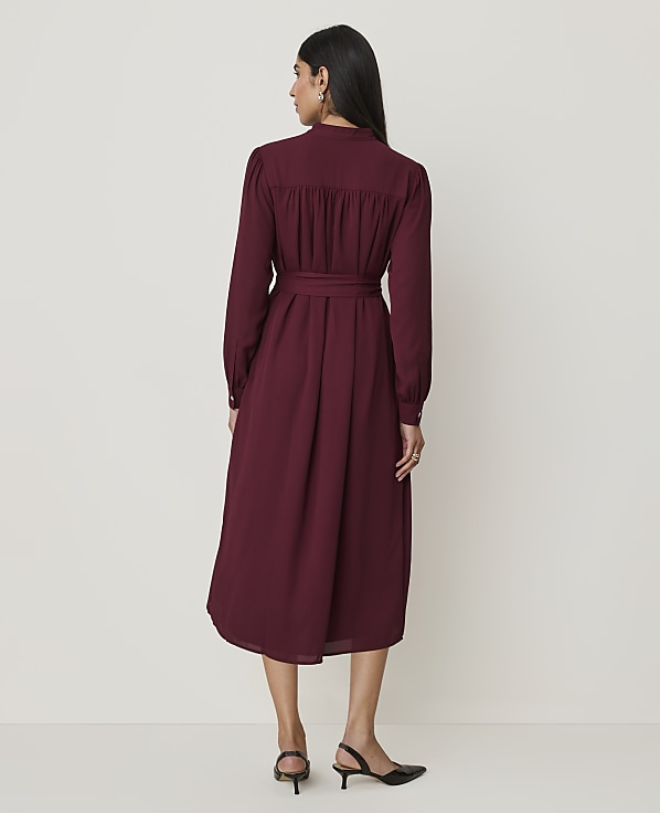 A woman in a burgundy dress stands against a plain, light-colored background.
