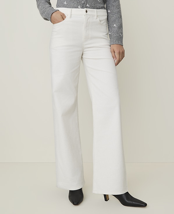 A person wearing white wide-leg pants and black heeled boots stands against a plain, light-colored background.