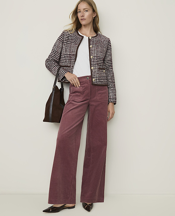 A woman in a tweed jacket and wide-leg corduroy pants stands against a plain, light-colored background.
