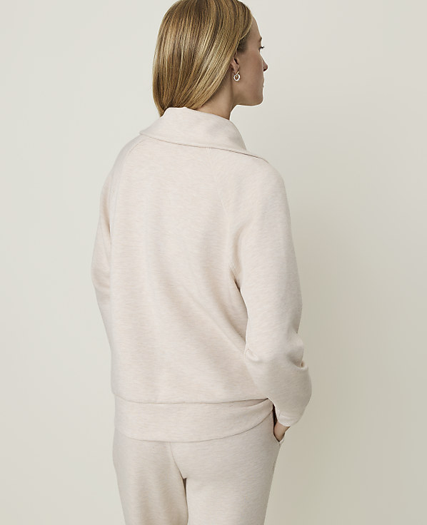 A woman in a light pink sweater and pants stands with her back to the camera against a plain, light-colored background.