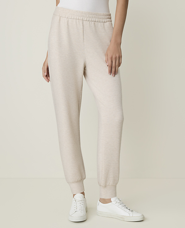 A person stands in light-colored sweatpants and white sneakers against a plain, light background.