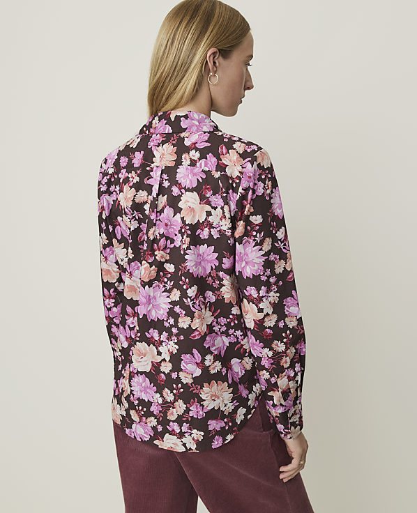 A woman in a floral print shirt stands against a plain, light-colored background.