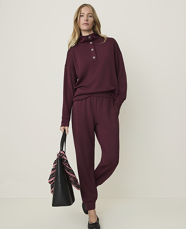 A woman in a burgundy loungewear set stands with a tote bag in front of a plain, light-colored background.