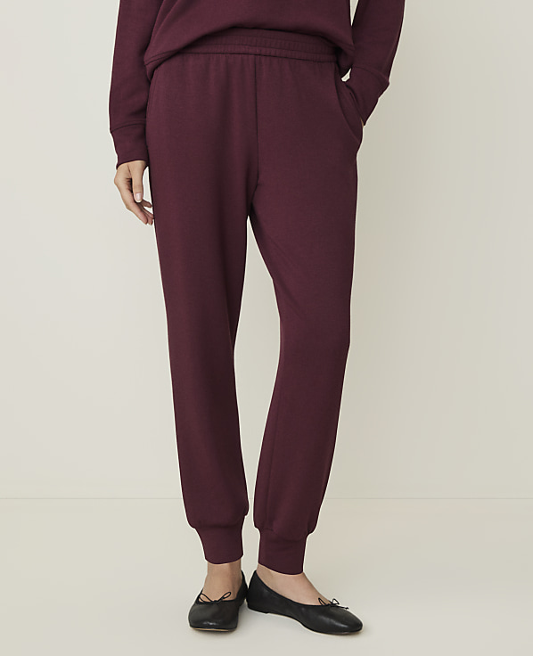 A person wearing burgundy sweatpants and black ballet flats stands against a plain, light-colored background.
