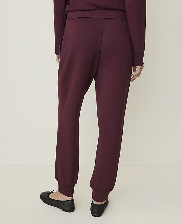 A person wearing burgundy sweatpants and black ballet flats stands against a plain, light-colored background.