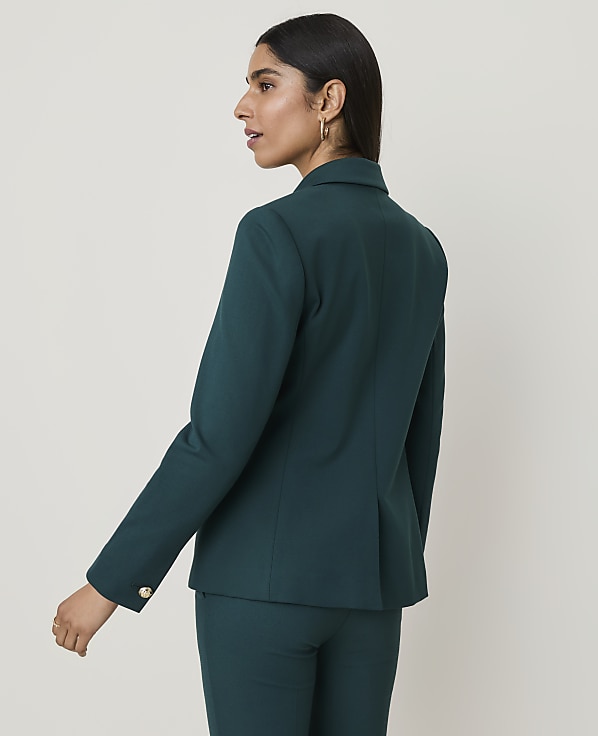 A woman in a teal blazer and pants stands against a plain white background.