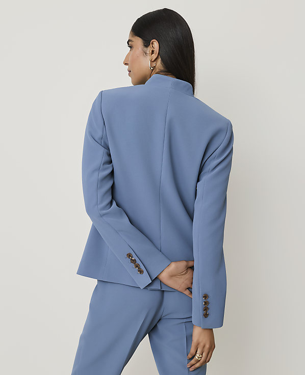 A woman in a blue blazer and pants sits against a plain, light-colored background.