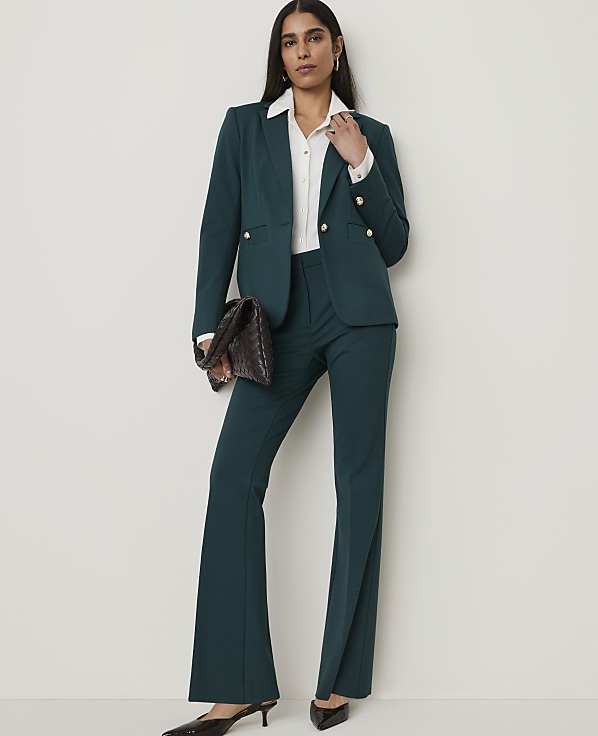 A woman in a teal pantsuit stands against a plain, light-colored background.