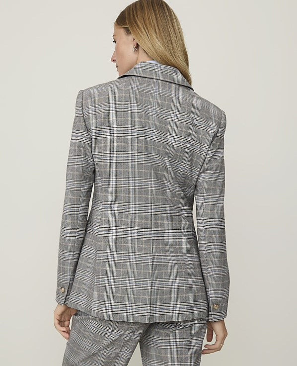 A woman in a grey plaid blazer and pants stands against a plain white background.