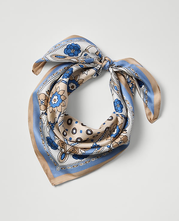 A patterned silk scarf with blue and tan floral designs is tied in a knot against a plain white background.