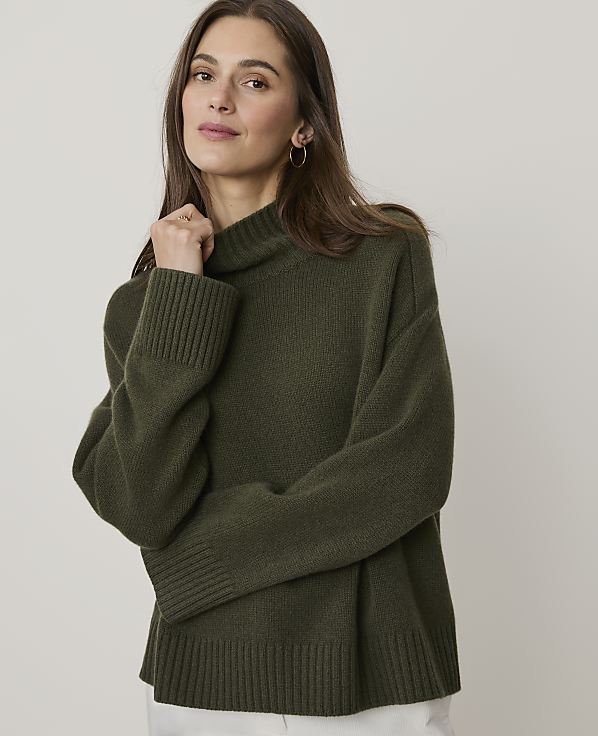 A woman in a green turtleneck sweater poses against a plain, light-colored background.