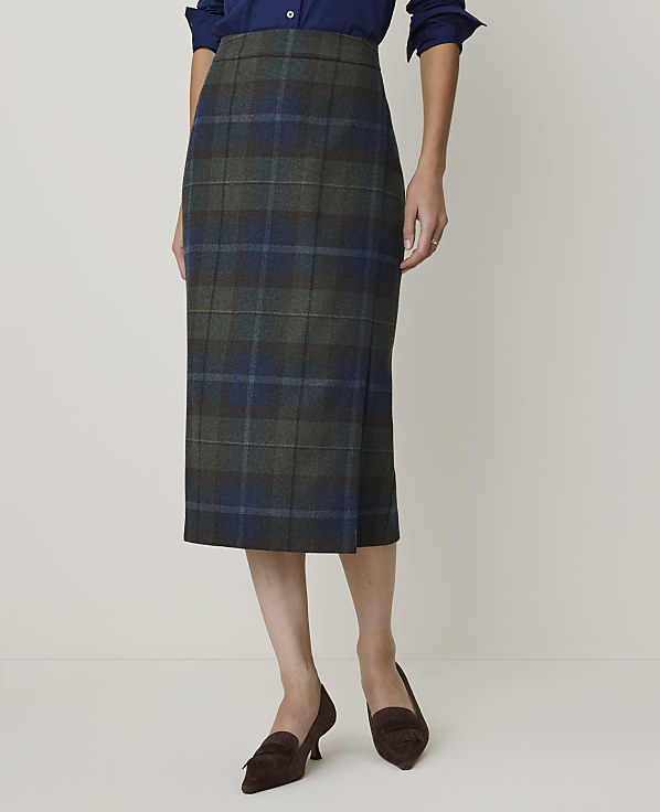 A woman models a green and blue plaid pencil skirt with brown loafers against a plain, light background.