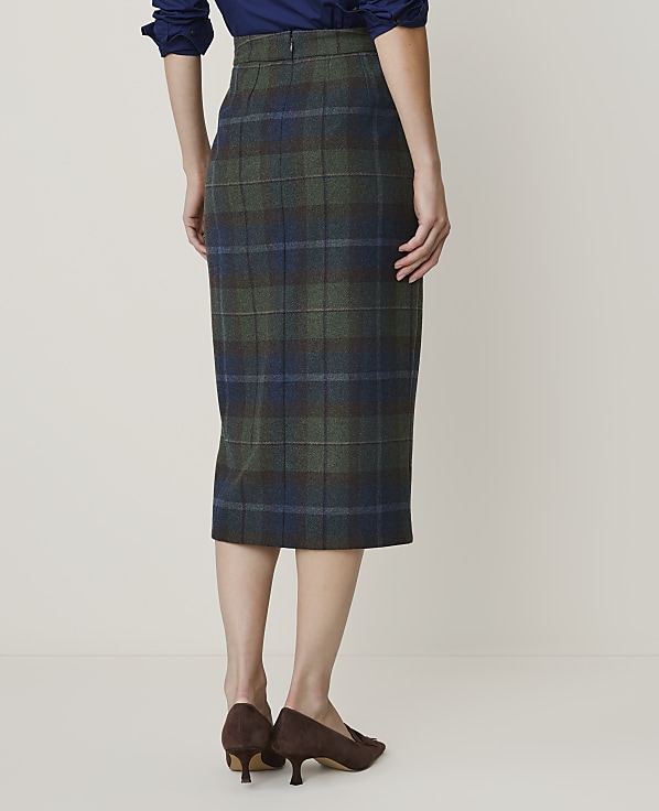 A woman in a plaid pencil skirt and brown heels stands against a plain, light-colored background.