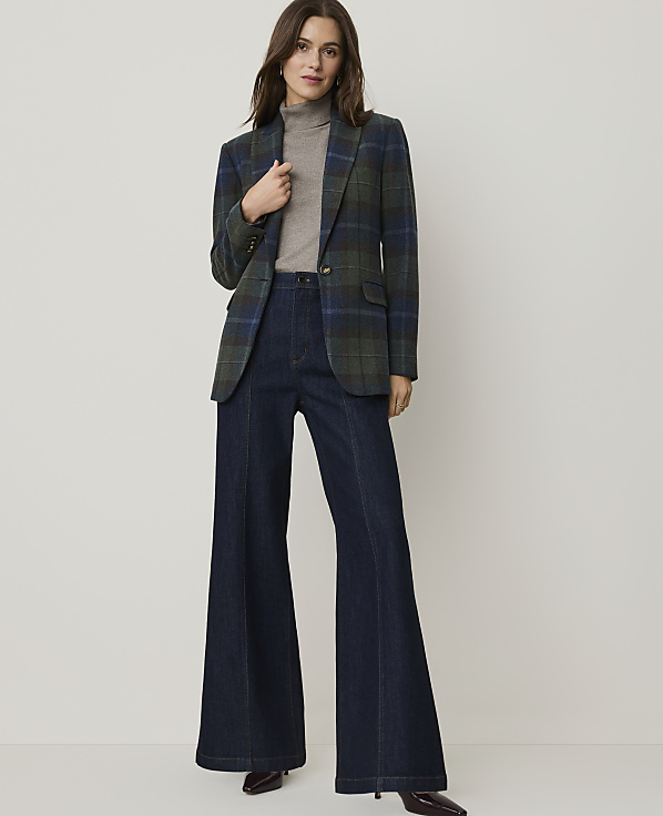 A woman in a plaid blazer and wide-leg jeans stands against a plain, light-colored background.