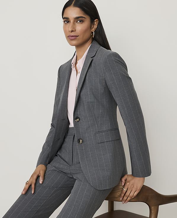 A woman in a pinstripe suit and pink blouse poses against a plain, light-colored background.