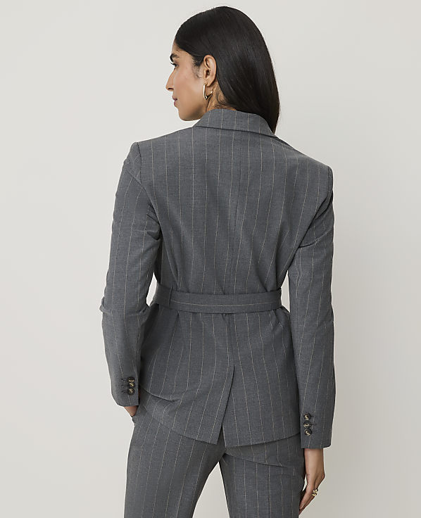 A woman in a pinstripe suit stands against a plain, light gray background.