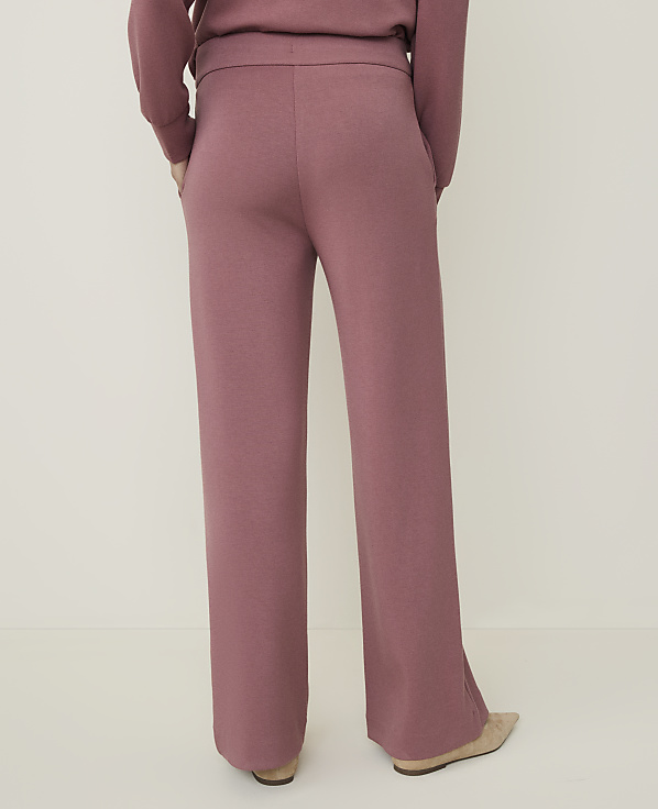 A person wearing rose-colored knit pants stands against a plain, light-colored background.