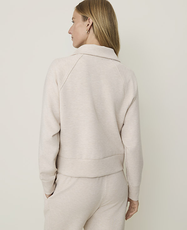 A woman in a cream-colored sweatshirt and pants stands against a plain, light-colored background.