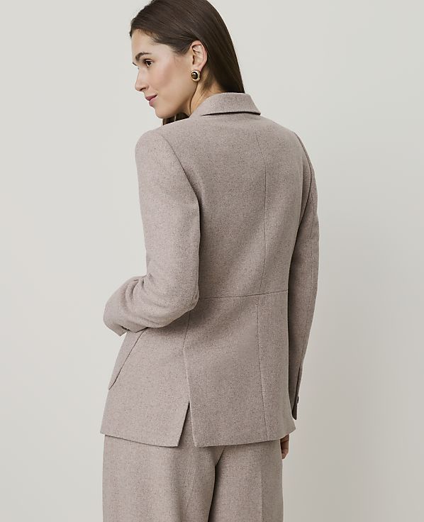 A woman in a beige blazer and pants stands against a plain, light-colored background.