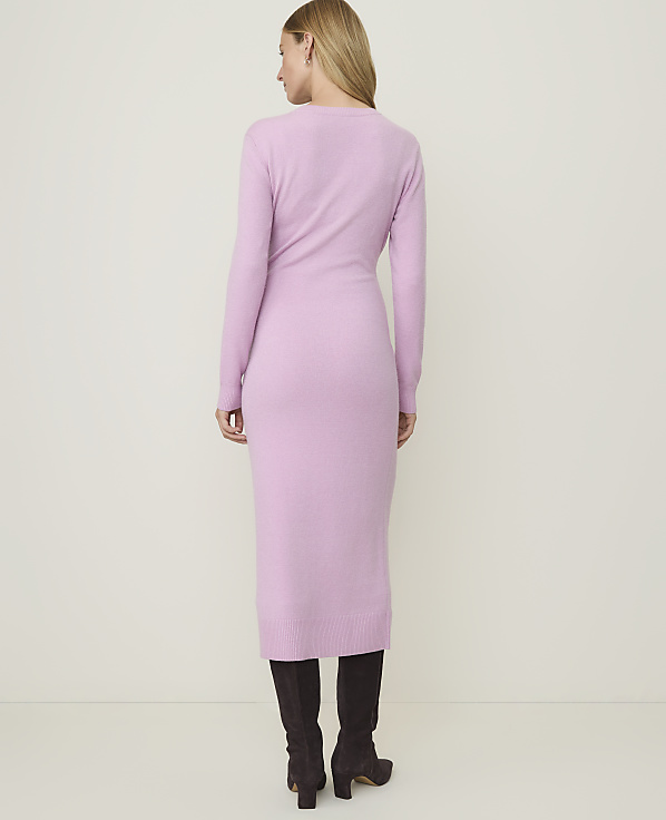 A woman in a pale pink midi dress and dark boots stands against a plain, light-colored background.