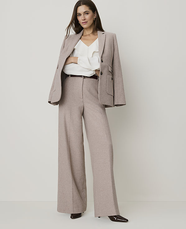 A woman in a beige pantsuit stands against a plain white background.