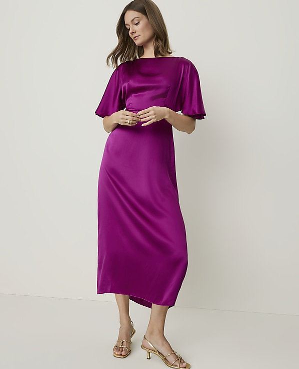 A woman in a vibrant magenta satin dress stands against a plain, light gray background.