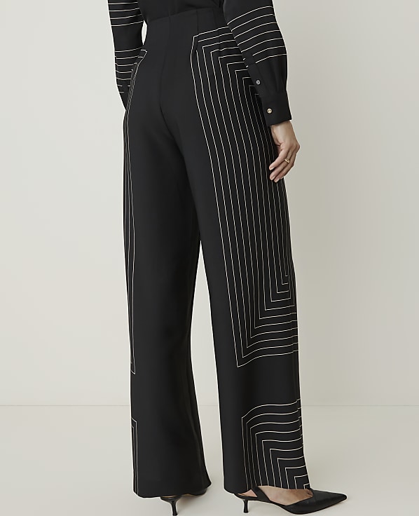 A person wearing black wide-leg pants with geometric white stitching stands against a plain white background.