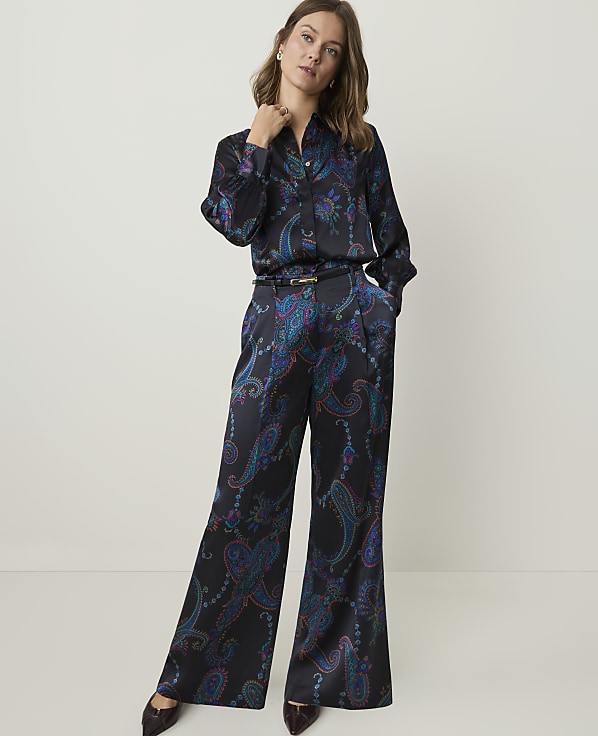 A woman in a patterned silk pajama set stands against a plain, light gray background.