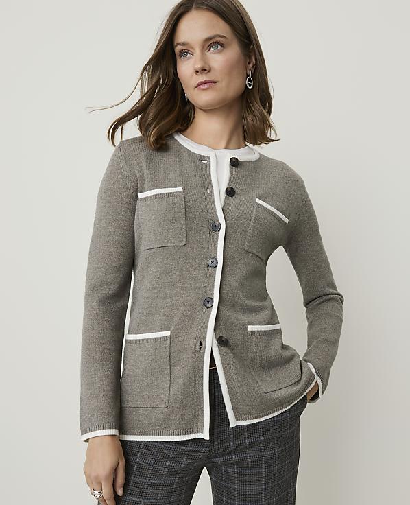 A woman in a grey cardigan with white trim and plaid pants stands against a plain white background.