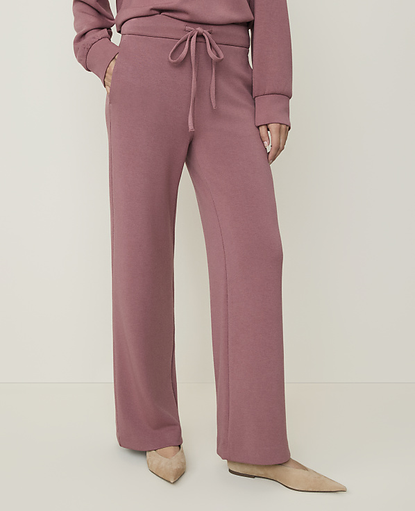 A person wearing rose-colored lounge pants and beige flats stands against a plain, light-colored background.