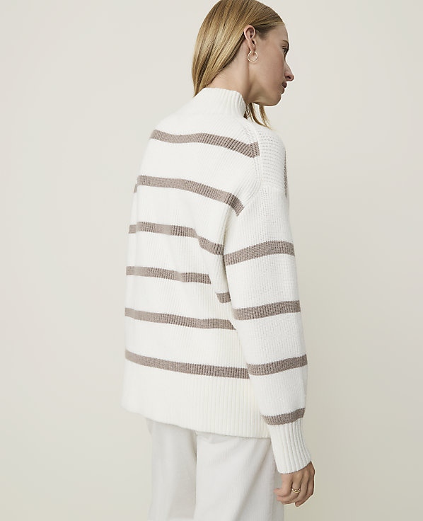 A woman in a white and brown striped sweater stands against a plain, light-colored background.