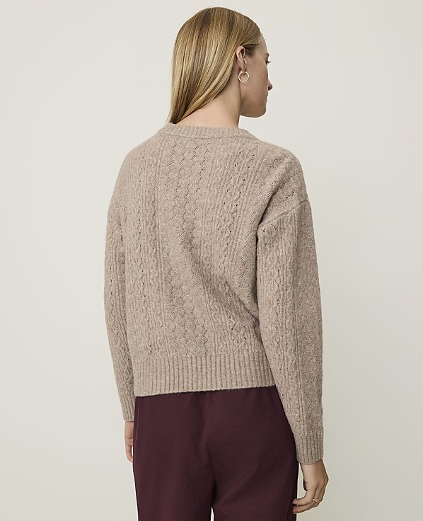 A woman in a cable-knit sweater stands against a plain, light-colored background.