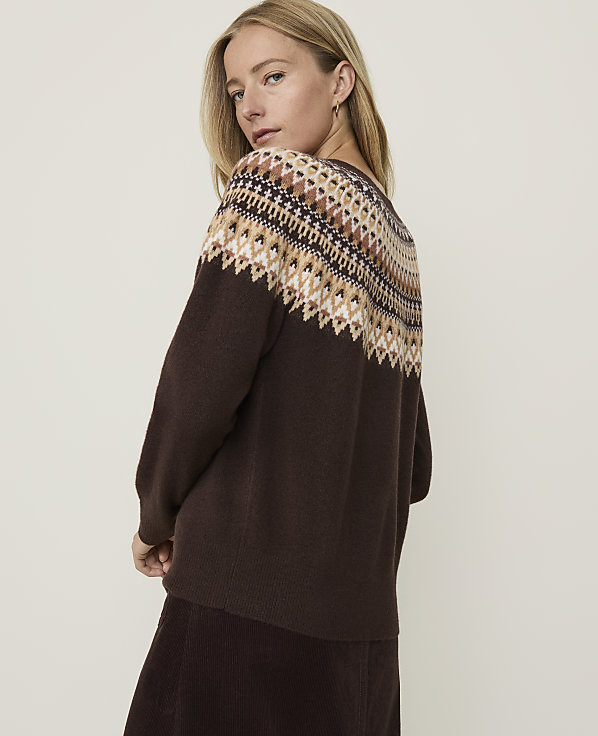 A woman in a brown sweater with a fair isle pattern stands against a plain, light brown background.