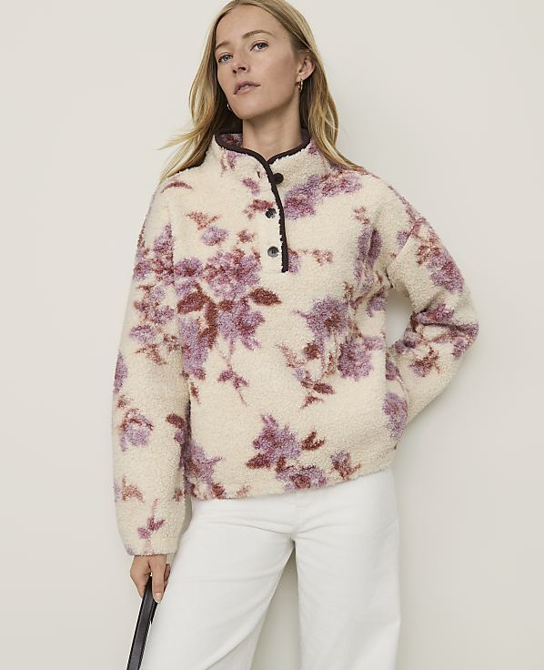 A woman in a cream-colored floral fleece pullover stands against a plain, light-colored background.