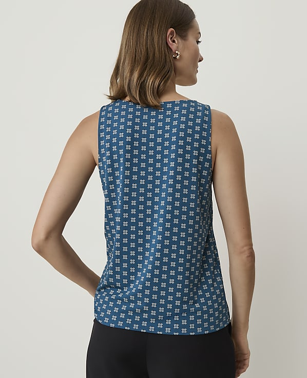 A woman in a teal patterned sleeveless top stands with her back to the viewer against a plain, light background.